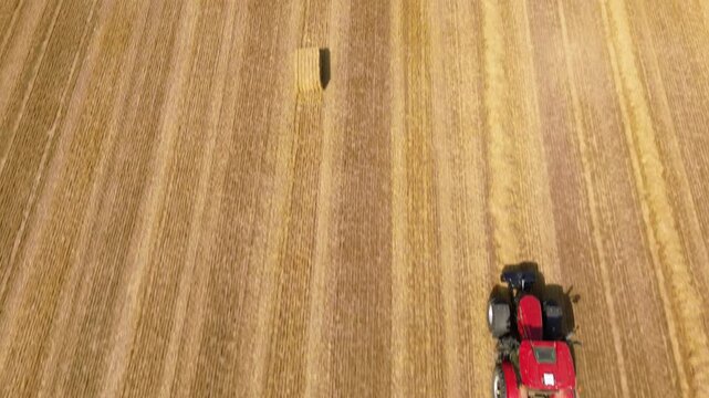 Aerial view of red square baler machinery baling straw on farmland after harvest