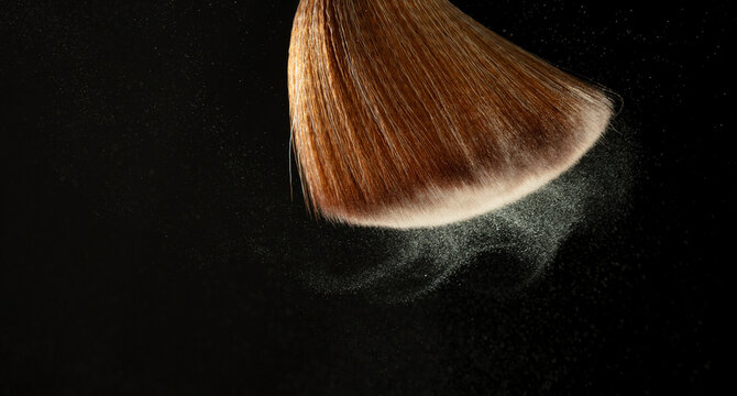 Big Soft Makeup brush with powder explosion. Cosmetic brush splash powder dust with glitter sparkling for make up. Black background isolated on photo element