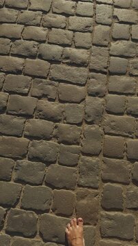 Bare foot walking on weathered stone pavement with strong sunlight and rustic texture