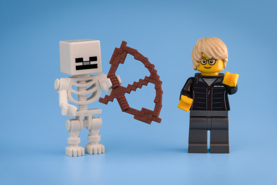 Minecraft Skeleton holding a brown Bow stands beside a blond yellow toy Lego minifigure wearing glasses and dark clothing against a light blue background on Jul 25, 2026 in Jakarta, Indonesia
