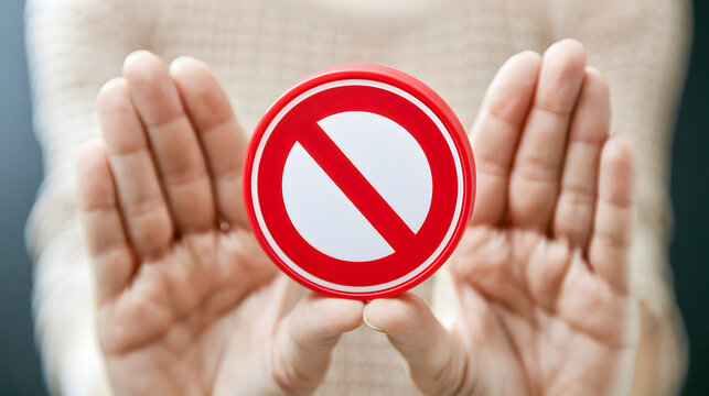 The close-up view of hands holding a red prohibition sign for a ban restriction warning and basic safety communication
