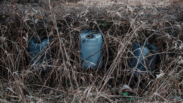 Discarded plastic containers hidden inside dry overgrown field with pollution environment discarded container contamination environmental landscape plasticware