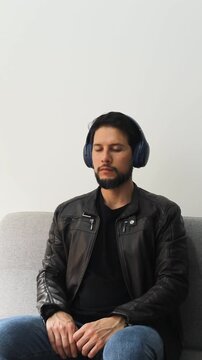 Vertical detailed view of a man with the eyes closed wearing a leather jacket sitting on a couch listening music on a wireless headset