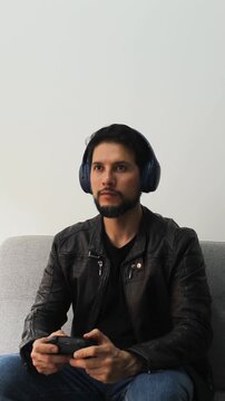 vertical detailed view of a latin gamer man wearing a leather jacket playing with a wireless controller in a concentrating attitude