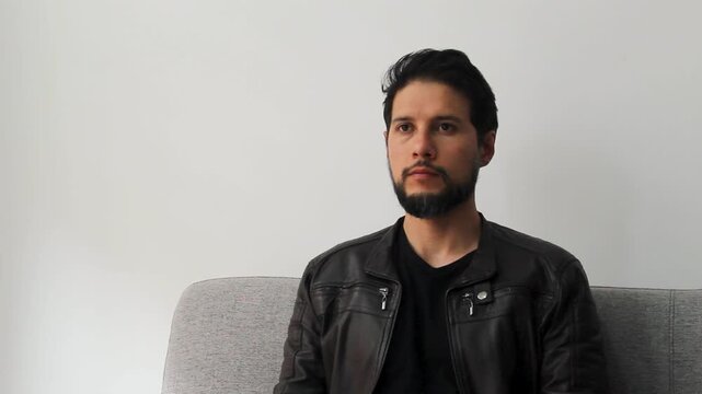 Detailed view of a caucasic male wearing a leather jacket sitting on a couch seeing to the front in a concentrating attitude