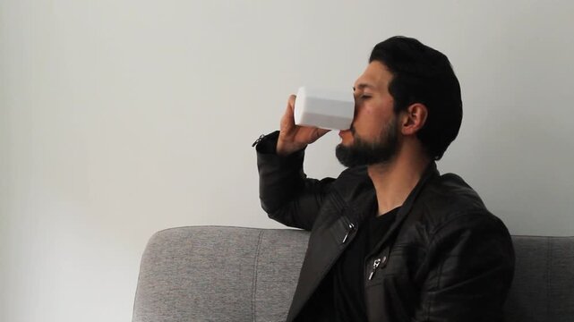 Detailed view of a latin man at the right side of the screen with a leather jacket drinking a a beverage in a reflexive attitude