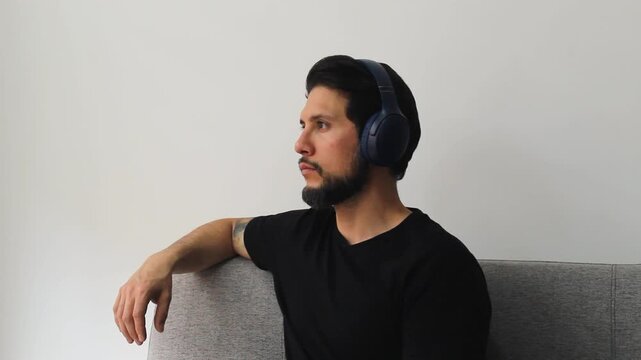 Detailed view of a caucasic male in a peaceful attitude sitting on a couch hearing something on a wireless headset