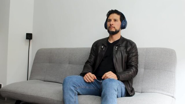 Detailed view of a latin man wearin leather jacket sitting on a couch listening music in a peaceful attitude