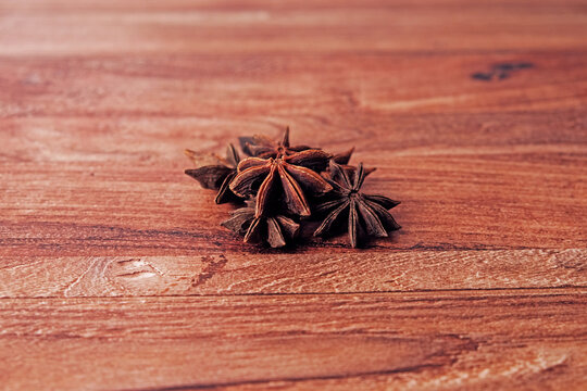 Star anise pods rest on warm wooden surface. Dark brown spice forms star shape. Texture and color highlight natural ingredients. Perfect for food, recipe, or cooking design