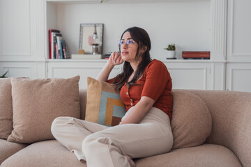 Young woman relaxing on couch at home looking thoughtful while lounging with a cushion © Daniel