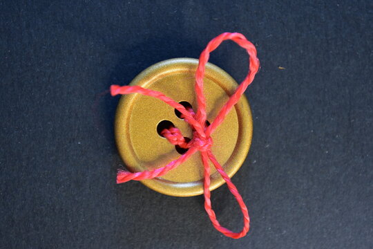 Gold button tied with pink thread on a dark background  