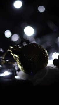 Una toma de cerca de unos adornos de navidad de varios colores con luces de navidad en un fondo negro. Video Vertical