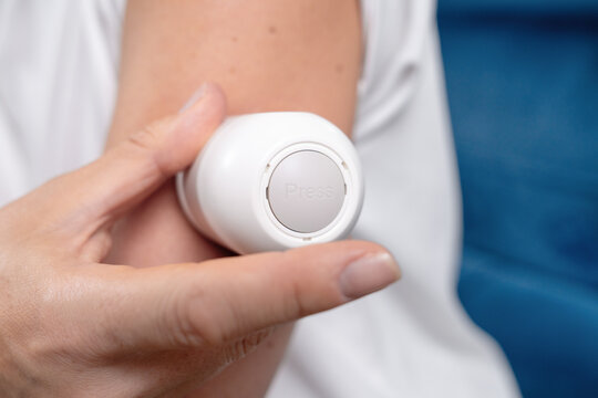 Woman hand holding a round white sensor applicator close to her bare upper arm ready to attach a glucose monitoring device. 