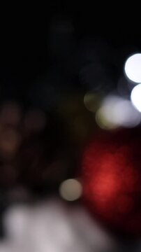Una toma de cerca de unos adornos de navidad de varios colores con luces de navidad con desenfoque en un fondo negro. Video Vertical