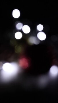 Una toma de cerca de unos adornos de navidad de varios colores con luces de navidad con desenfoque en un fondo negro. Video Vertical