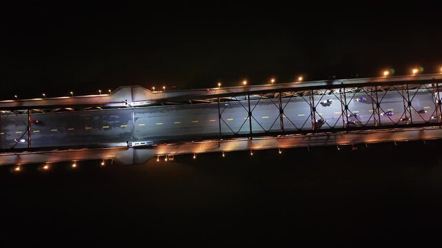 Aerial perspective of a busy bridge at night, featuring vehicles in motion under bright lights, highlighting urban traffic dynamics and vibrant colors