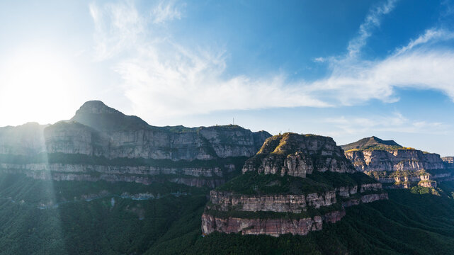 Layered rocky mountain cliffs under a bright blue sky with sunlight illuminating the landscape. 