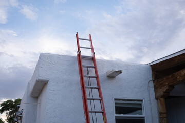 Red ladder leans against textured white wall. Clouds drift above the construction site © Salted Bytes 