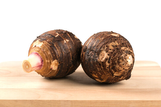 Two organic raw taro corms placed on wooden cutting board, isolated on white background. Culinary, agriculture, and healthy ingredient concepts.