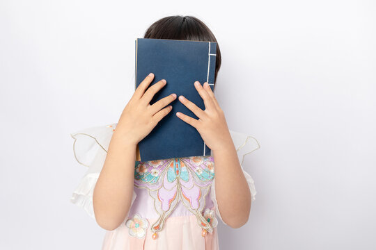 A young girl wearing Hanfu reading a book against a white background