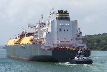 Fototapeta premium Stern perspective of an LNG carrier assisted by a tugboat during transit through the Panama Canal. Modern shipping and energy transportation.