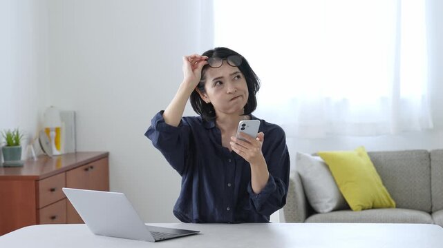 困った表情でパソコンとスマートフォンを使う中高年女性