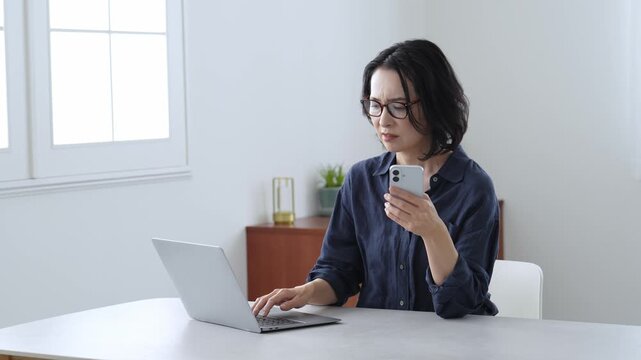 困った表情でパソコンとスマートフォンを使う中高年女性