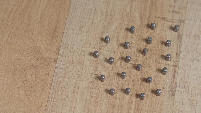 Small lead pellets for air gun arranged in pattern on light wooden tabletop video slow motion concept