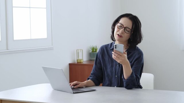 困った表情でパソコンとスマートフォンを使う中高年女性