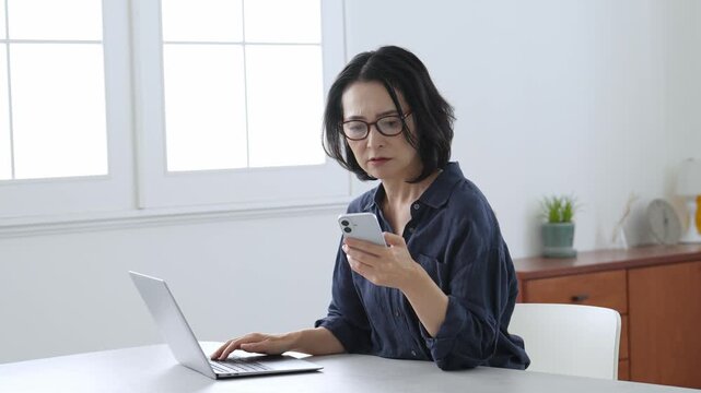 困った表情でパソコンとスマートフォンを使う中高年女性