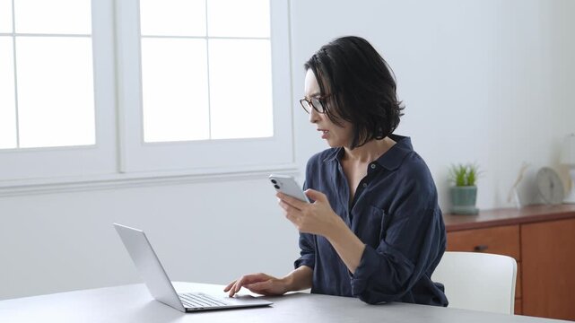 困った表情でパソコンとスマートフォンを使う中高年女性