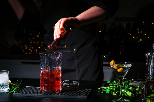 Expert bartender pouring red liquor from copper jigger into mixing glass. Professional mixology craft concept.