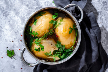 Fototapeta na wymiar Cooked jacket potatoes with fresh herbs and peppercorns in pot