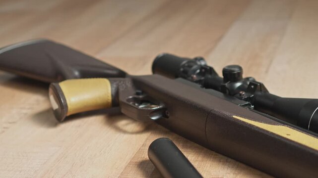 Close-up of tactical air rifle with optical scope and detached suppressor on wooden floor
