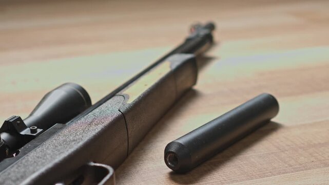 Close-up of air rifle with scope and silencer lying on wooden table