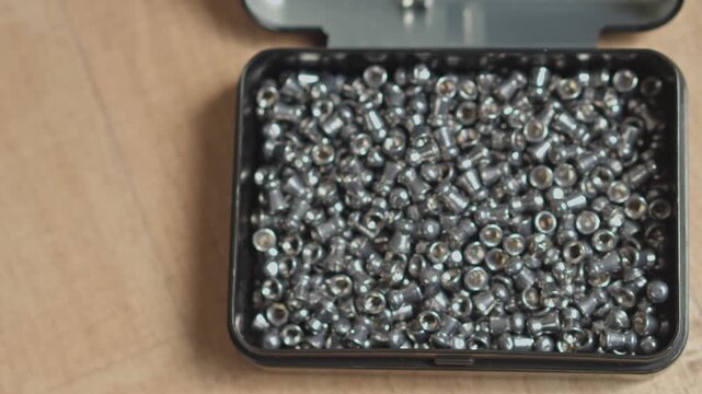 Overhead close-up of metallic air rifle ammunition loaded inside small storage tin