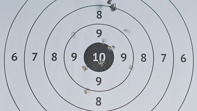 Overhead slow-motion view of airgun ammunition dropping across scored paper shooting target with existing bullet holes
