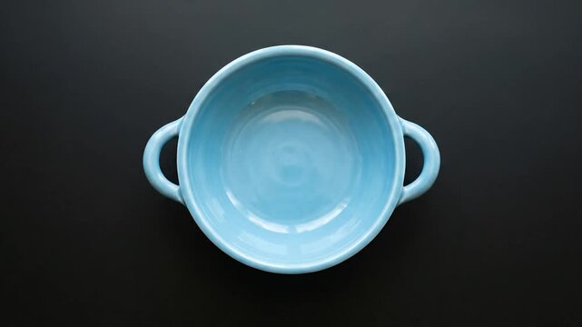 Empty light blue ceramic bowl with dual handles on a dark background.