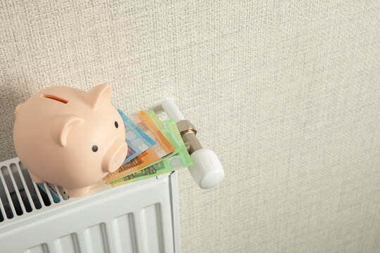 Heating season. Piggy bank rests on radiator with bank notes nearby