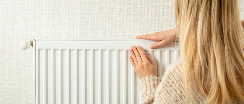 Heating season. Woman touches radiator in cozy home while ensuring warmth during heating season