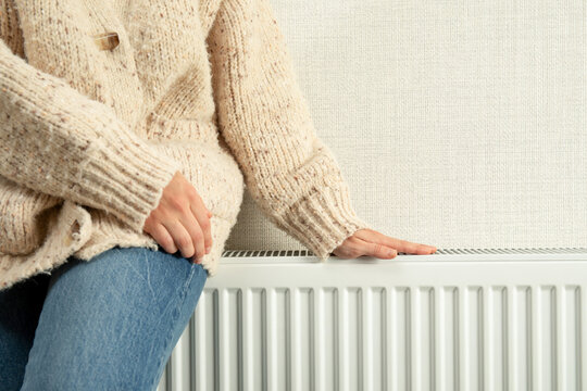 Heating season. Person relaxes at home, enjoying warmth from radiator on a chilly day