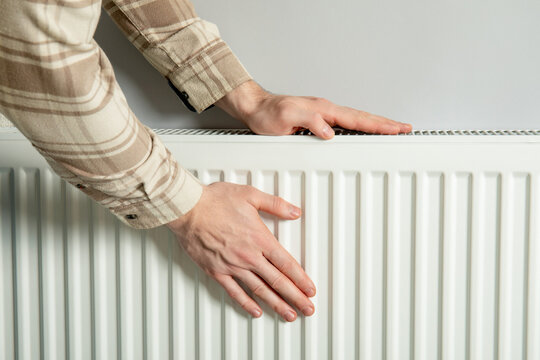 Heating season. Hands press against radiator to feel warmth during heating season