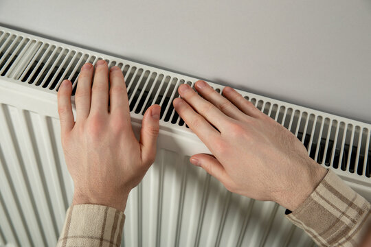 Heating season. Person warms hands on radiator in residential space. Heating season comfort concept