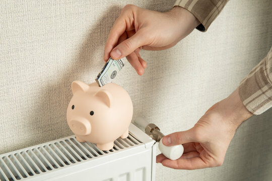 Heating season. Individual places money into piggy bank while adjusting radiator valve