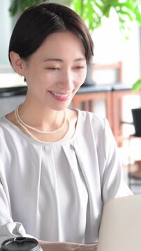 A Japanese woman working on her laptop in a stylish, bright office; Office Work & Business Scenes (Vertical Video)