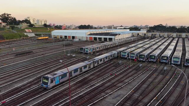 Aerial view of a metro train moving through a large railway depot at sunset