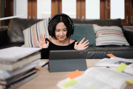 Asian teenage girl greeting in online class, remote learning at home using digital tablet, writing and reading textbooks, self-study for back to school, Homeschooling, university education lifestyle.