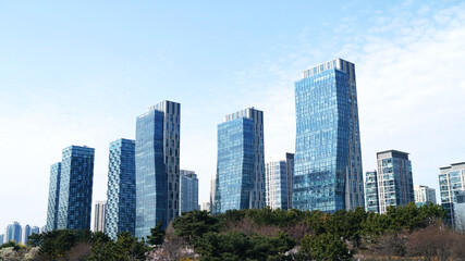 Fototapeta premium Modern glass office buildings in business district under a clear blue sky. Suitable for business, finance, architecture, urban development, real estate, smart city, and corporate presentation concepts