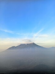 Fototapeta premium Volcano Peak at Sunrise with Sea of Clouds and Sun Rays in Blue Sky