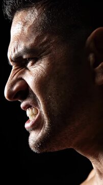 Close up profile of an angry man with gritted teeth showing intense emotion and aggression on a dark background